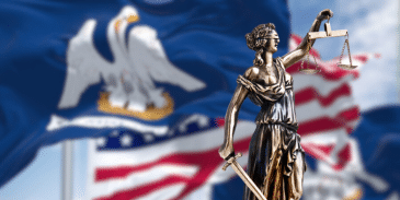 Bronze figure of Lady Justice with her scales on a background of the Louisiana State and United States flags waving in the wind